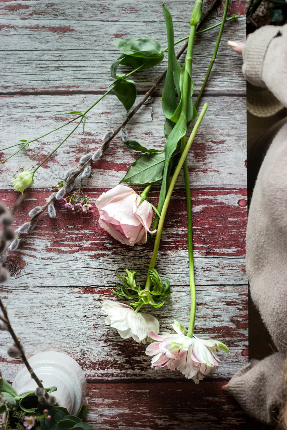 A rustic table, with flowers, roses to be exact and a woman working on on them